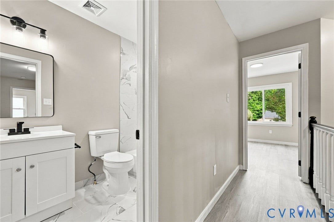5831 Larrymore Road, Richmond, VA 23225 Bathroom featuring a vanity with a rectangular sink, matte black faucet, and large wall mirror, complemented by wood-finish flooring, white stone-patterned wall tile, and a staircase with a white balustrade