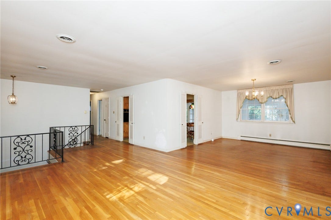 Open-concept interior featuring wood-finish flooring, decorative wrought iron railings, a multi-tiered chandelier, and dual sets of French doors