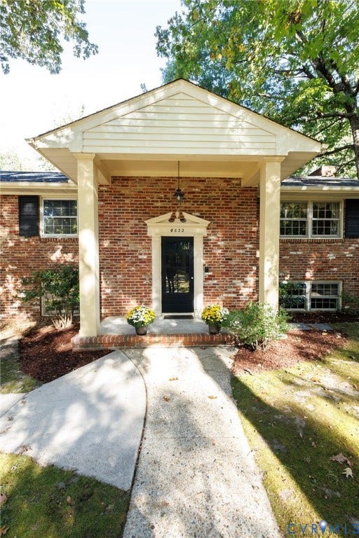 Brick exterior featuring a covered entryway with square columns, a pediment door surround, and multi-pane windows with dark shutters