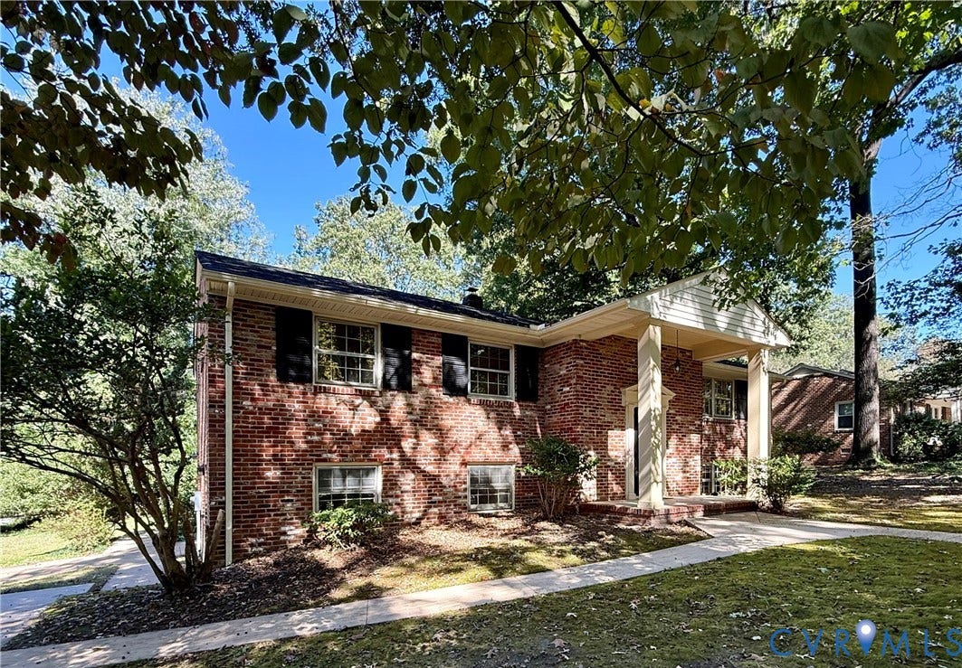 Brick exterior featuring a covered front porch with columns, shuttered windows, and a paved walkway