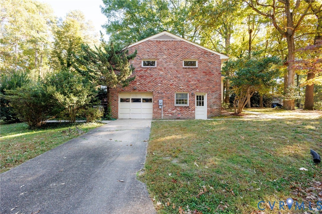 Multi-story brick exterior featuring a single-car garage, concrete driveway, and mature landscaping