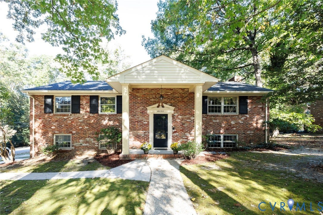 Brick exterior featuring a covered entryway with structural columns, multi-pane windows with shutters, and a front gabled roofline