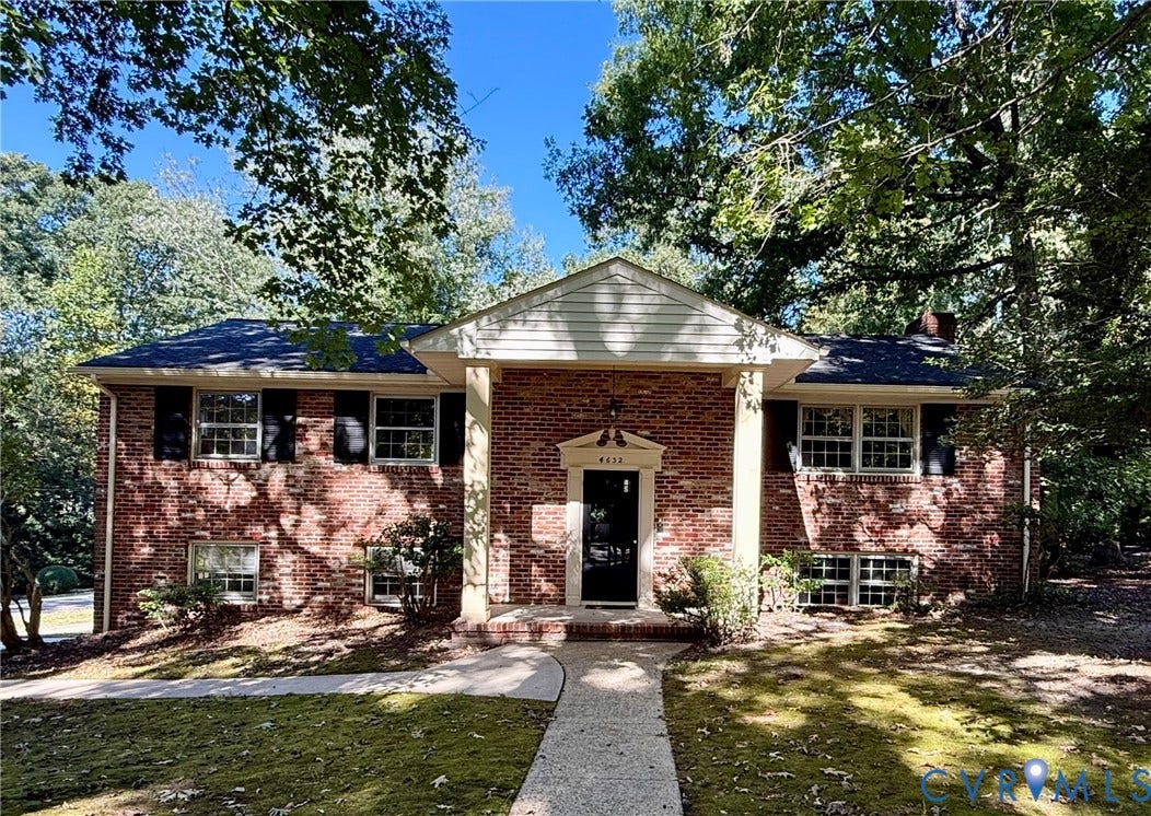 Two-story brick exterior featuring a prominent covered entryway with tapered columns, multipane windows, and dark shutters