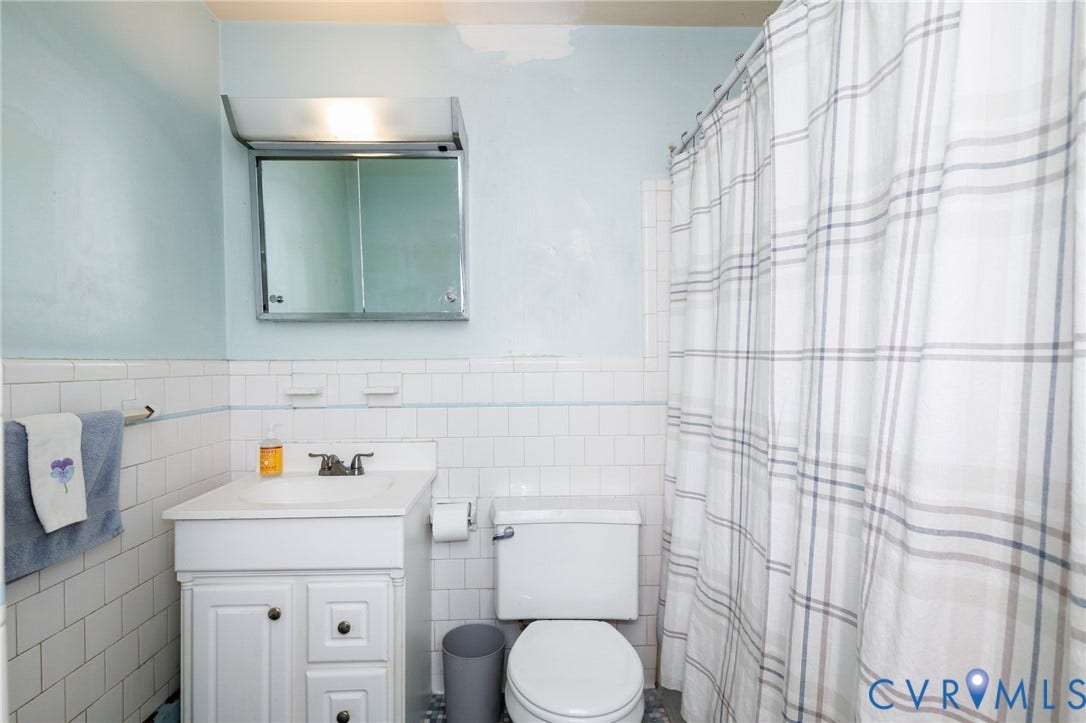 Bathroom featuring white subway tile wall cladding, vanity with integrated basin and storage cabinetry, medicine cabinet with surface-mounted lighting, and a bathtub enclosure