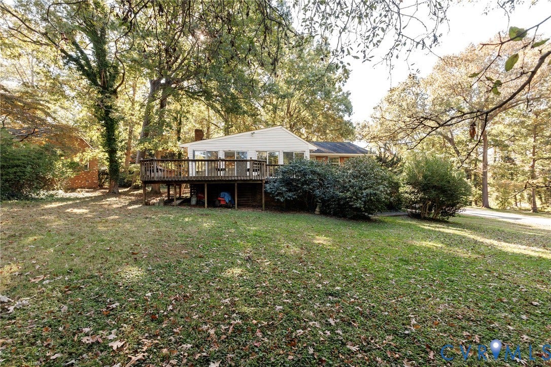 Rear exterior featuring a large elevated wood deck, siding facade, brick chimney, and expansive wooded grounds