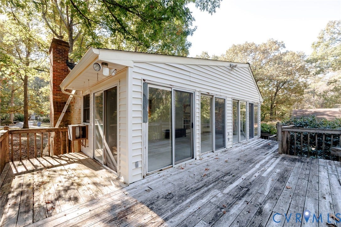 Exterior deck featuring wood-plank flooring, brick chimney, multiple sliding glass doors, and light-colored horizontal siding