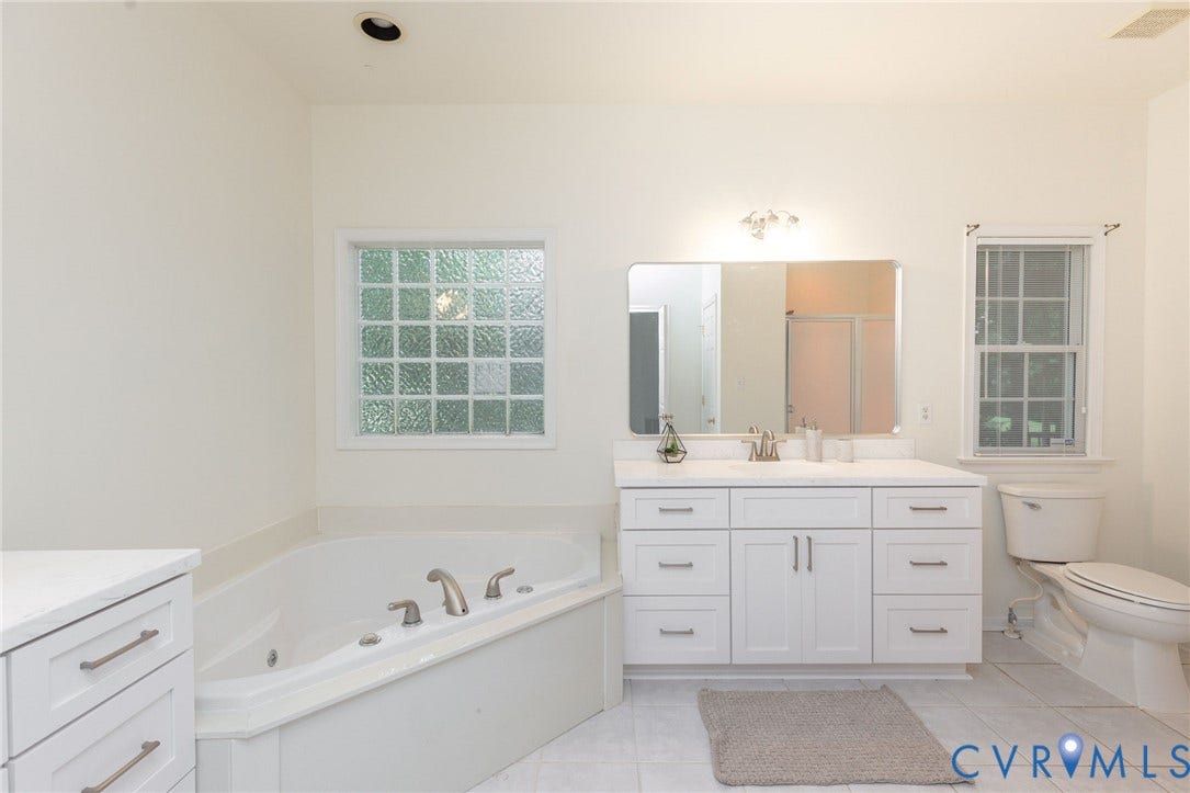 13742 Spyglass Hill Circle, Chesterfield, VA 23832 Corner soaking tub, white vanity with expansive countertop, large wall-mounted mirror, glass block window, and tile flooring