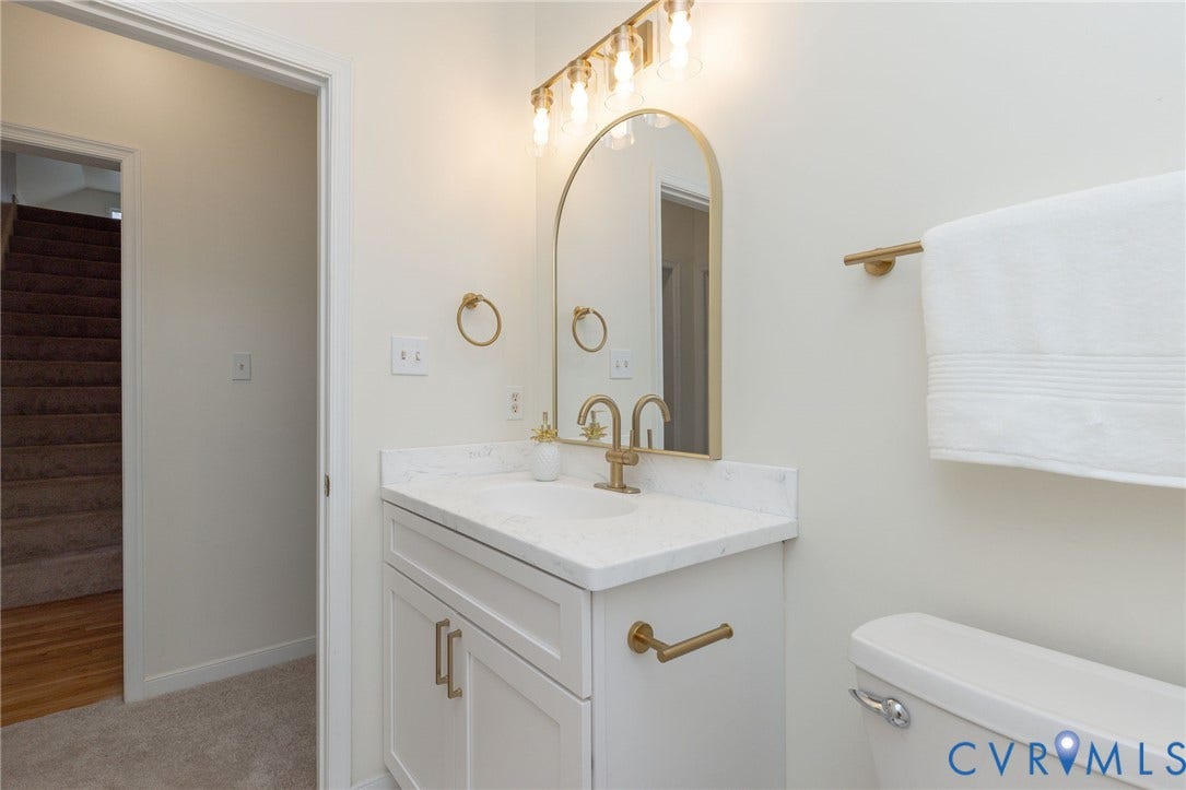 13742 Spyglass Hill Circle, Chesterfield, VA 23832 Bathroom vanity featuring a stone-look countertop, white Shaker-style cabinetry, an arched mirror, and brass-finish hardware and lighting fixtures