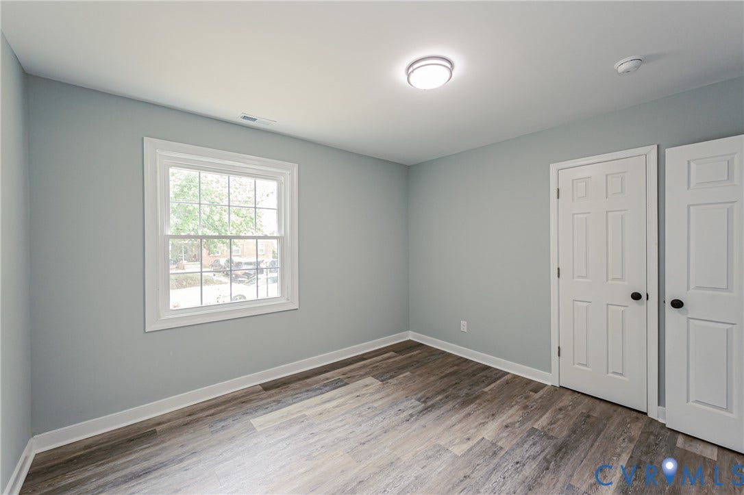 Light-filled room featuring wood-finish flooring, a white window, paneled doors with matte black hardware, and a flush-mount ceiling light