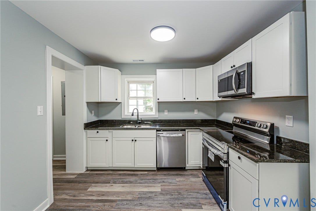 Kitchen featuring white cabinetry, dark stone countertops, stainless steel appliances, wood-finish flooring, and a single window