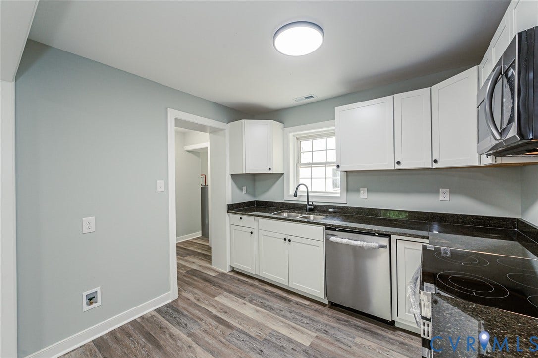 Kitchen featuring wood-finish flooring, white cabinetry, dark countertops, and stainless steel appliances