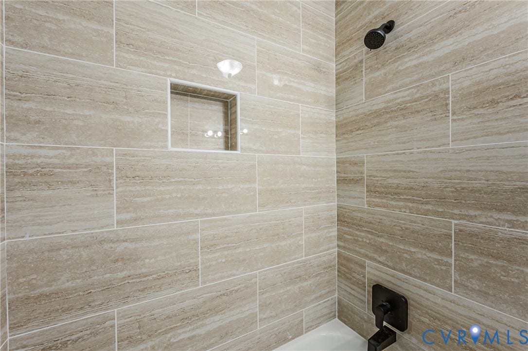 Tiled shower surround with a built-in niche, black finish shower head, and black finish shower controls