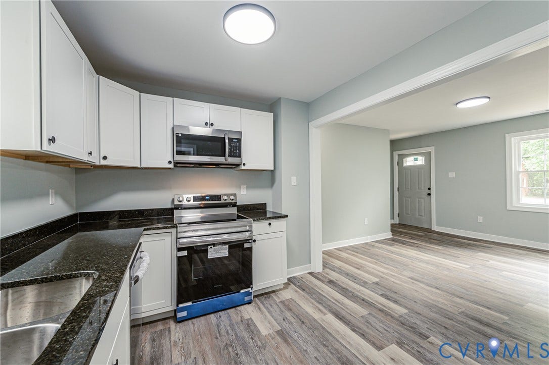 Kitchen featuring white cabinetry, dark countertops, stainless steel appliances, and wood-finish flooring