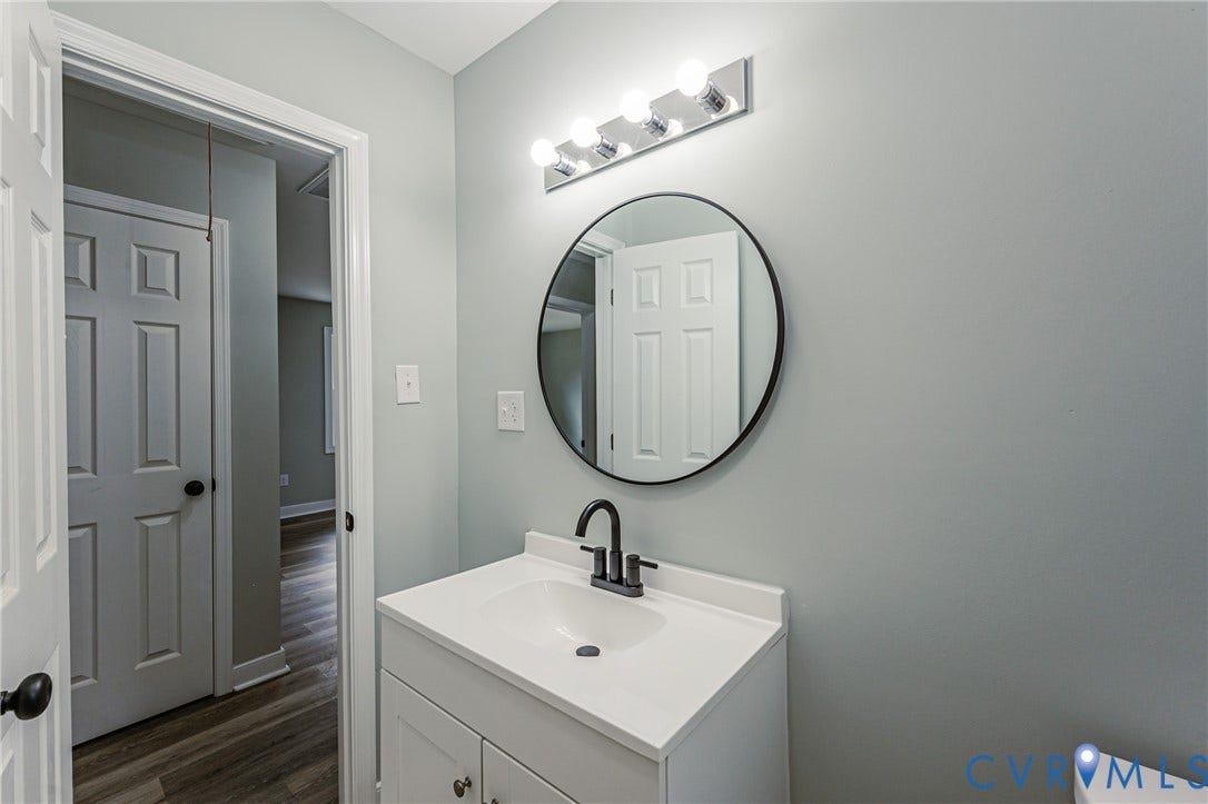White vanity with integrated sink, matte black faucet, and circular mirror