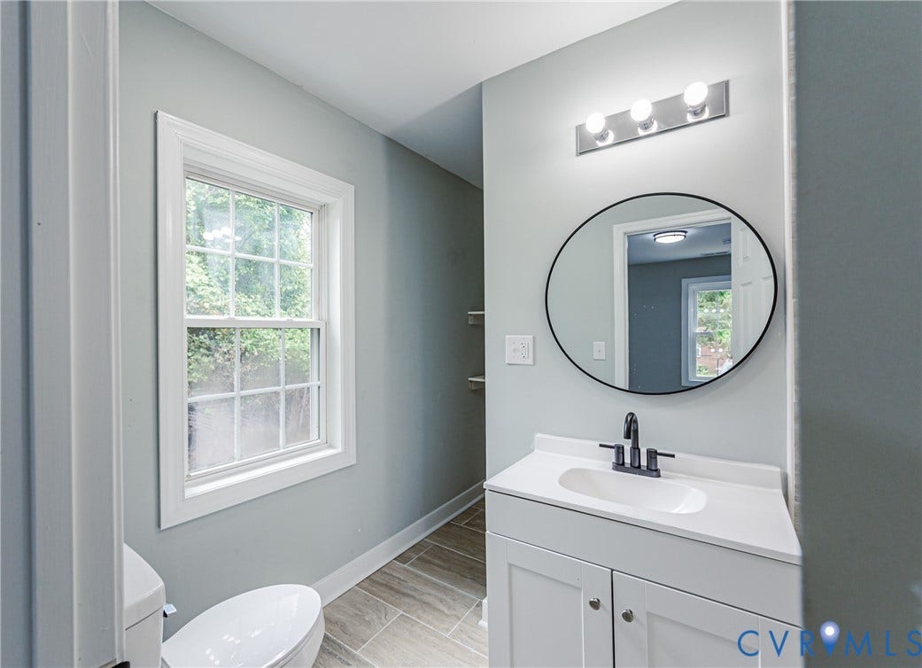 Bathroom featuring a white vanity with integrated sink, matte black faucet, and a round wall-mounted mirror