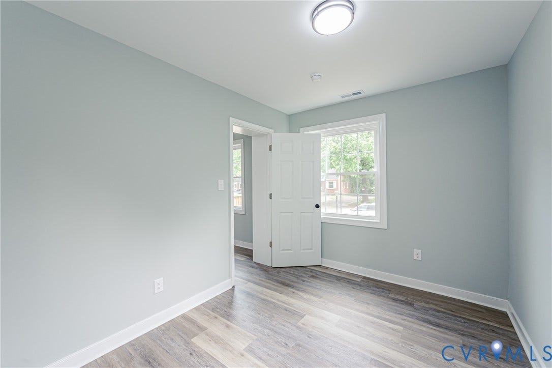 Wood-finish flooring, light blue wall paint, white trim, and a window with white casing
