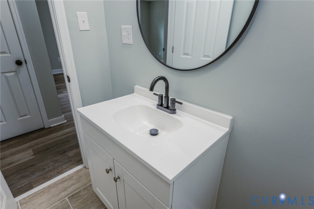White vanity with shaker-style cabinetry, matte black faucet, and a round black-framed mirror