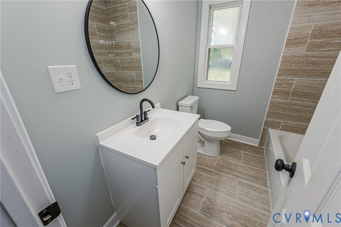Bathroom featuring a white vanity with integrated sink, black-finish faucet, framed circular mirror, and tile flooring