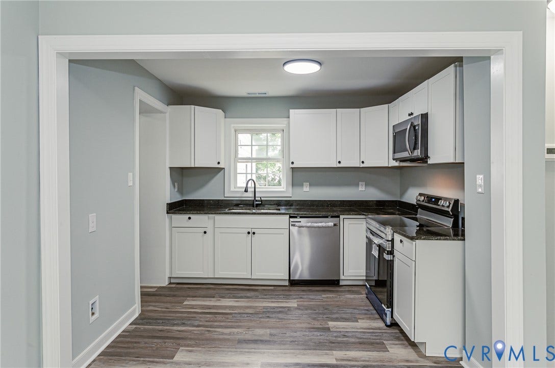 Kitchen featuring wood-finish flooring, white cabinetry, dark countertops, and stainless steel appliances