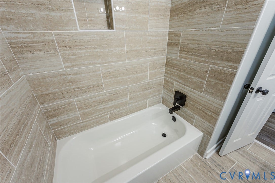 Bathtub with matte black fixtures, full-height tile surround, recessed tile niche, and coordinating tile flooring