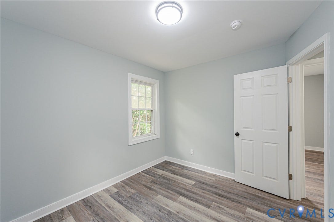 Wood-finish flooring, white trim, recessed window, and a paneled interior door with black hardware