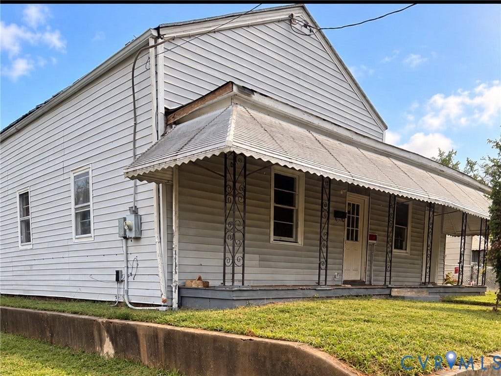 1400 N 29th Street, Richmond, VA 23223 Classic farmhouse featuring horizontal siding exterior, gabled roofline with metal accents, covered front porch with decorative support columns, multiple windows providing natural light, and manicured lawn with mature landscaping