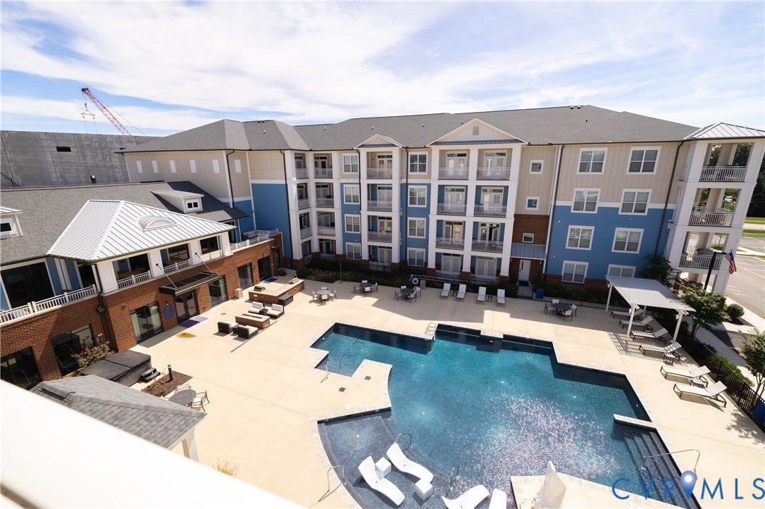 Multi-story building with balconies, an outdoor swimming pool, and a surrounding hardscape with lounge areas