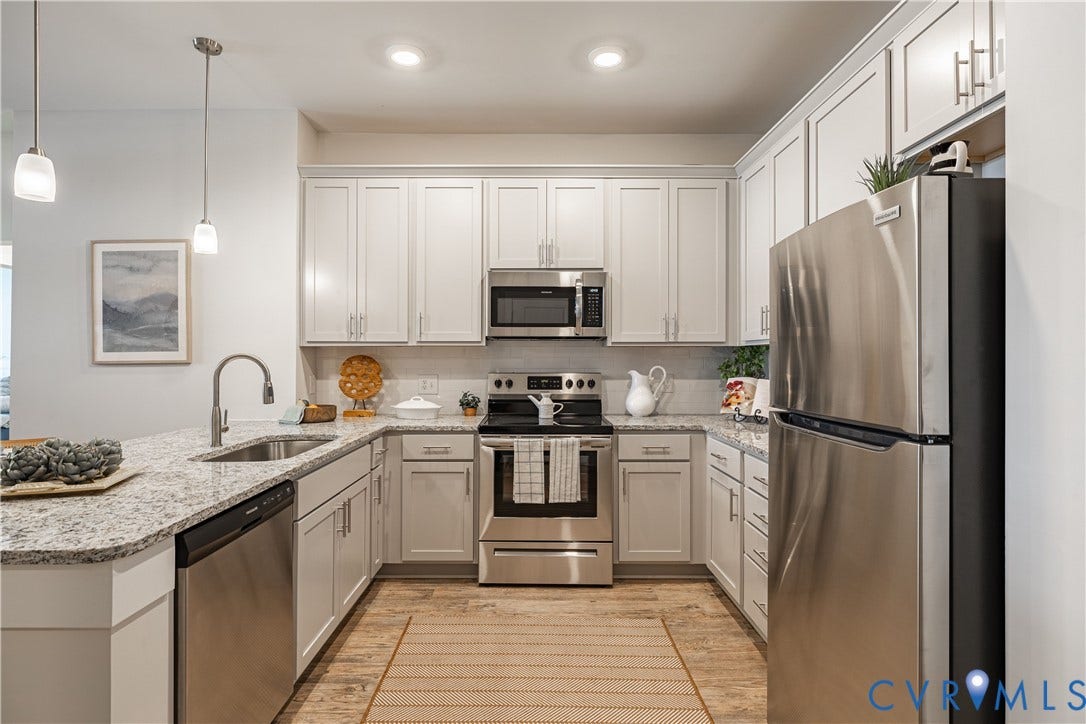 U-shaped kitchen featuring white cabinetry, stainless steel appliances, granite countertops, and wood-finish flooring