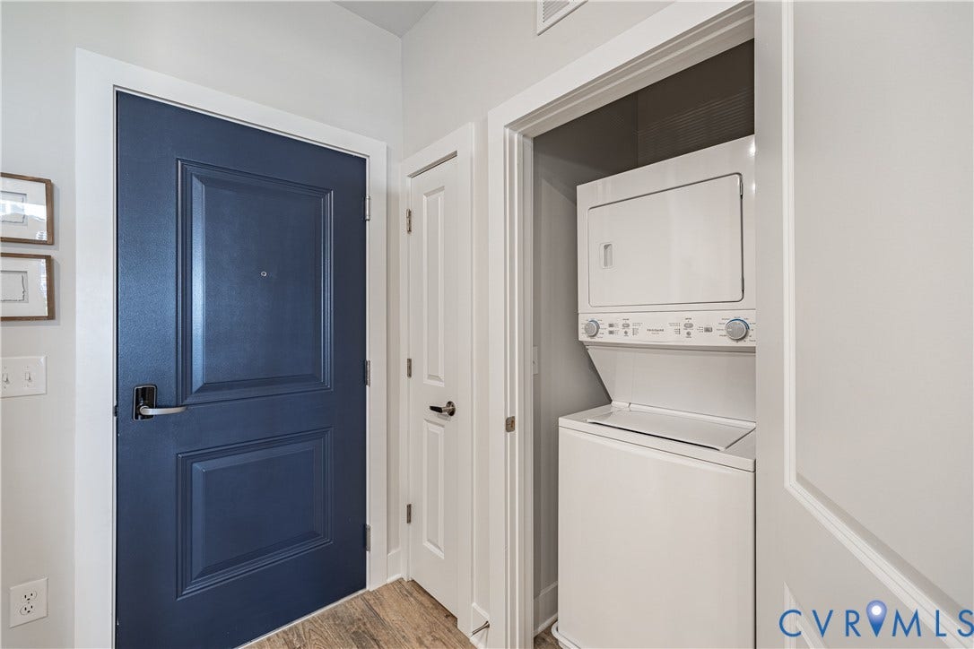 Panel-style entry door with matte black hardware, wood-finish flooring, and a stacked washer/dryer unit