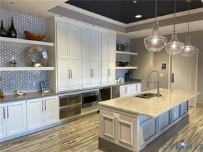 Large kitchen island with an undermount sink, pendant lighting, built-in appliances, white cabinetry, and wood-finish flooring