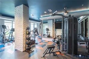 Fitness center featuring large windows, patterned flooring, a brick-textured column, and ceiling lighting
