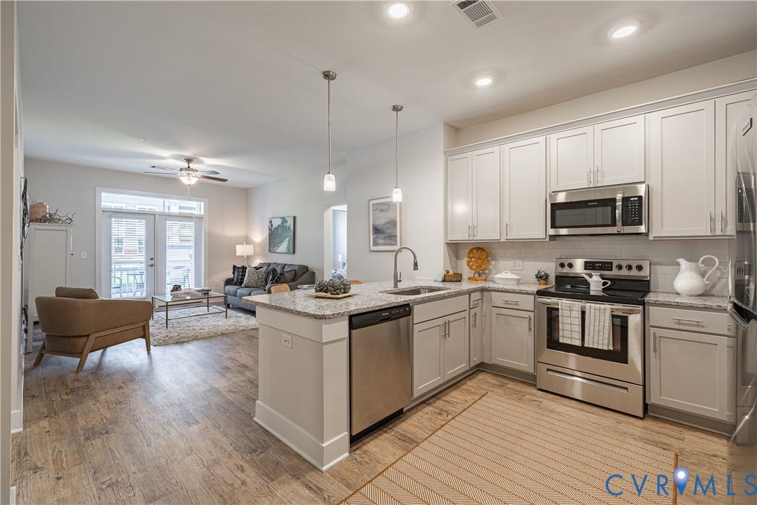 Open-concept kitchen featuring light-toned cabinetry, stainless steel appliances, and granite countertops with an integrated sink