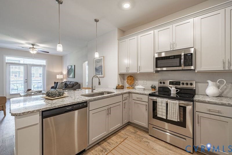 Kitchen featuring light-toned cabinetry, granite-style countertops, stainless steel appliances, a tile backsplash, and wood-finish flooring