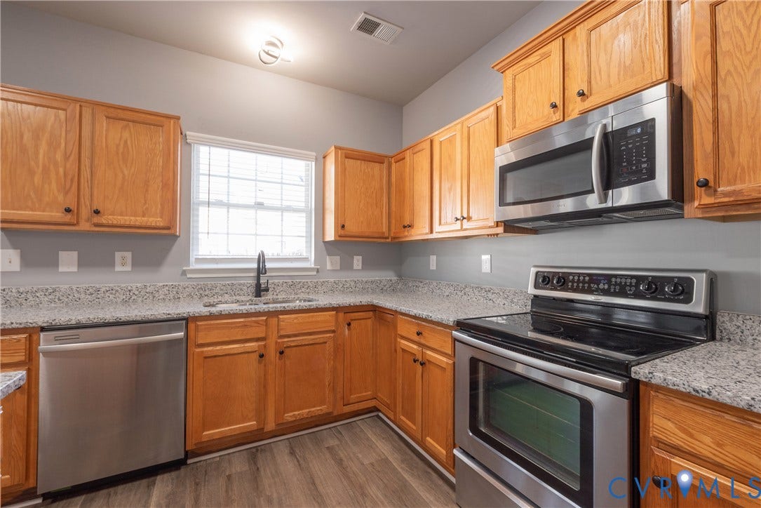 Kitchen featuring wood cabinetry, stainless steel appliances, speckled countertops, a window, and wood-finish flooring