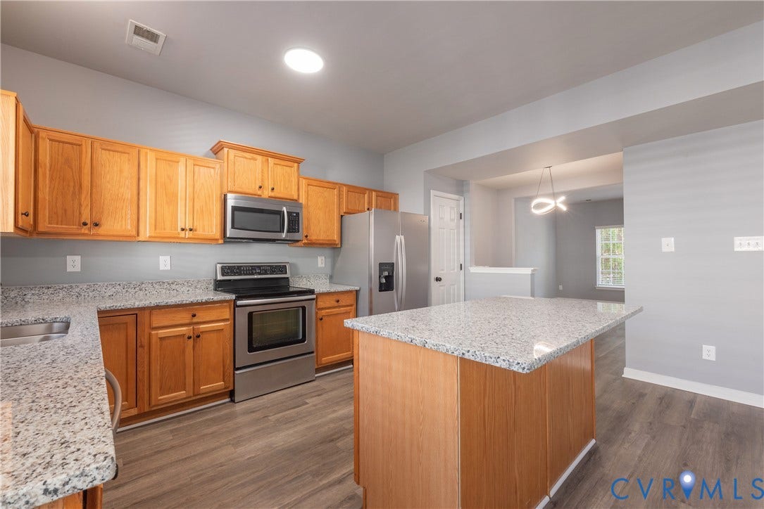 Kitchen featuring wood-finish cabinetry, stainless steel appliances, speckled countertops, a central island, and wood-finish flooring