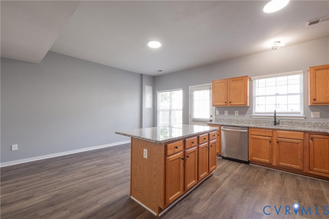 Kitchen island with access to family room with granite countertop, wood-finish cabinetry, stainless steel dishwasher, and wood-finish flooring