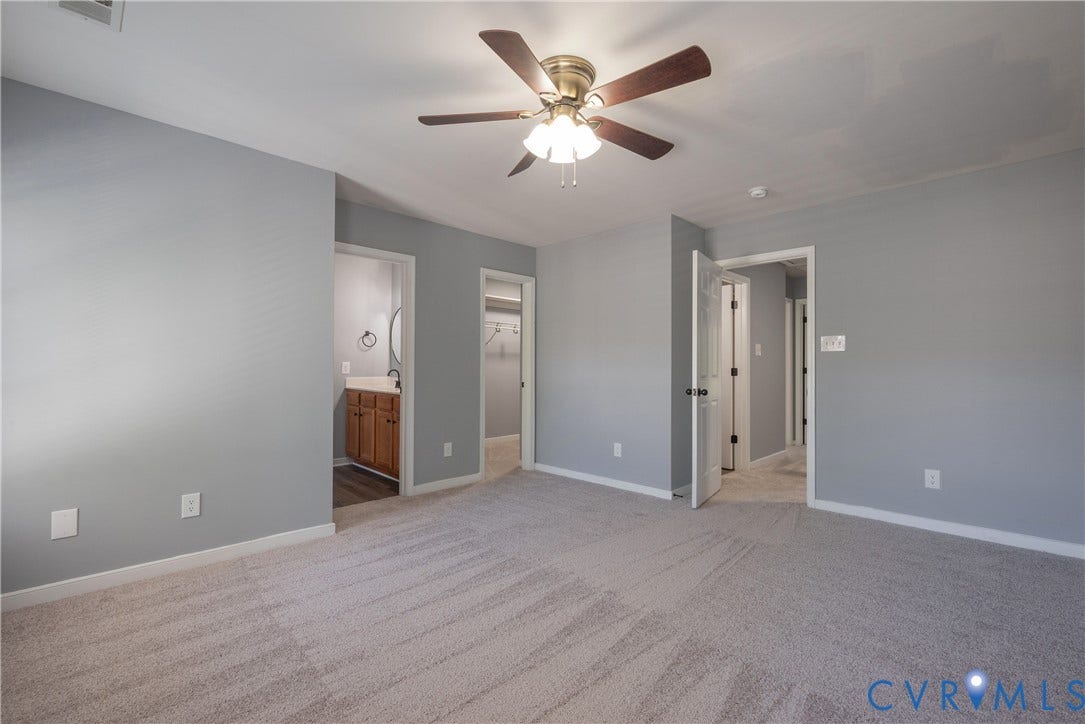 Carpeted room with a ceiling fan, light gray wall color, and white trim with walk in closet and full bath