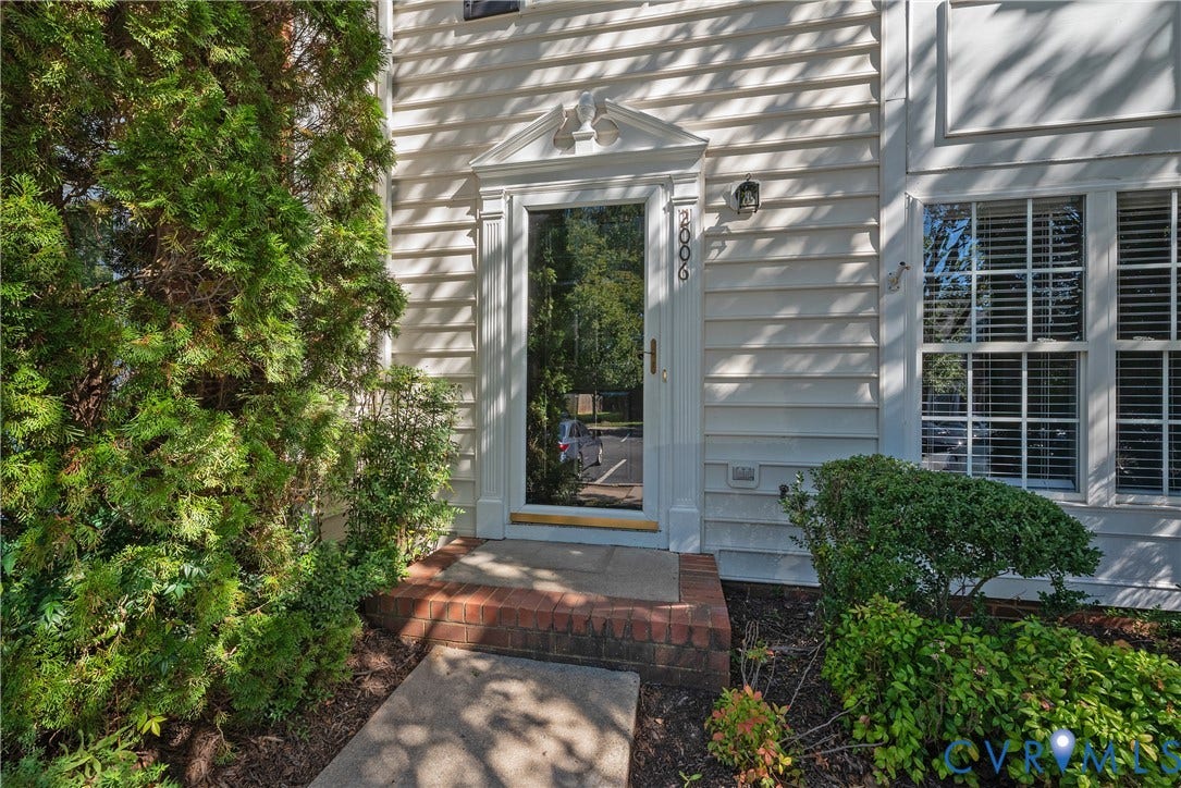 Entryway featuring white siding, brick detailing, a full-lite door, and an exterior wall lantern