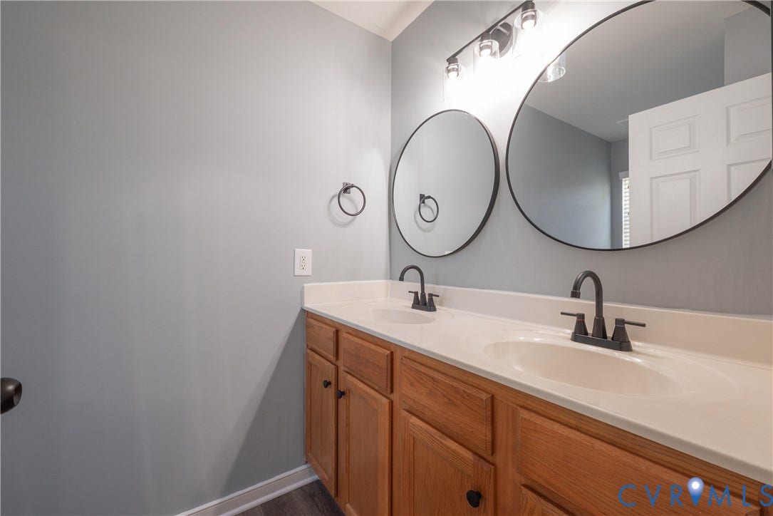 Dual vanity with undermount sinks, wood-finish cabinetry, matte black faucets, and round framed mirrors