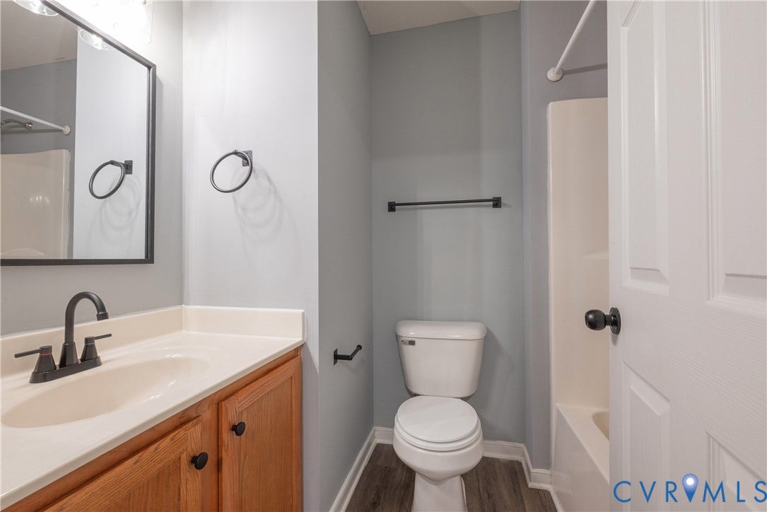 Hall bath with Neutral wall color, wood-finish flooring, white vanity countertop, matte black fixtures, and a shower/tub combination