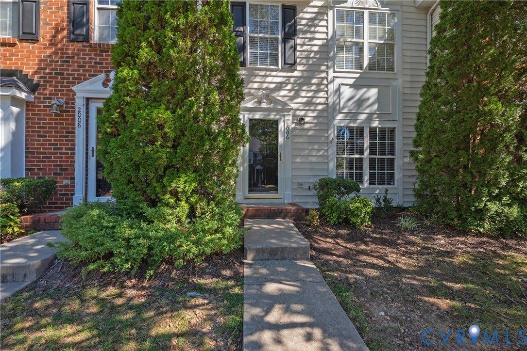 Siding exterior with black shutters, mature landscaping, and a concrete walkway
