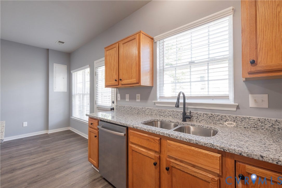 Kitchen featuring wood-finish cabinetry, granite-style countertops, double stainless steel sink, and stainless steel dishwasher