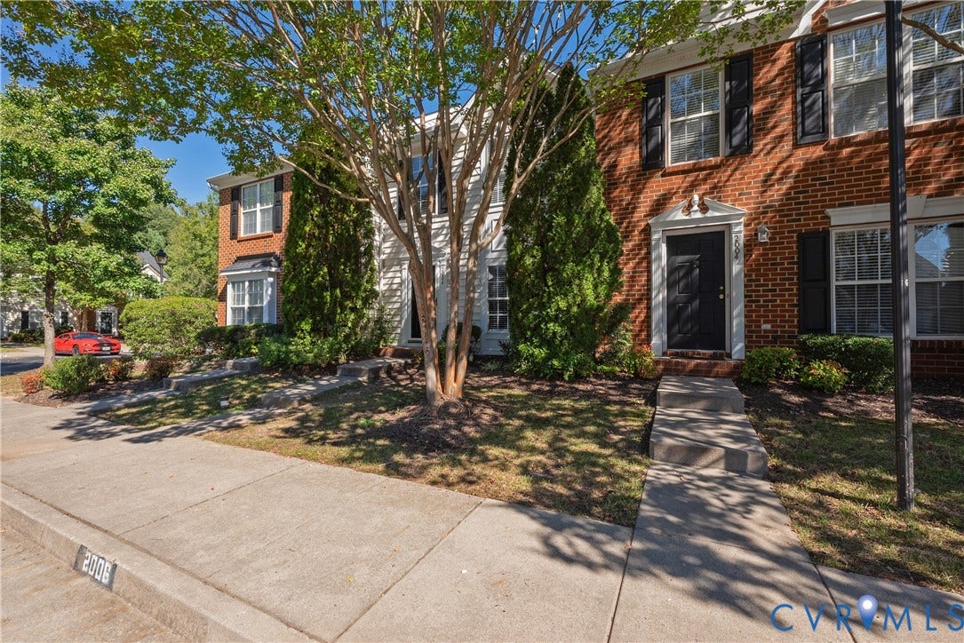 Brick and siding exterior with black shutters, mature trees, and landscaping