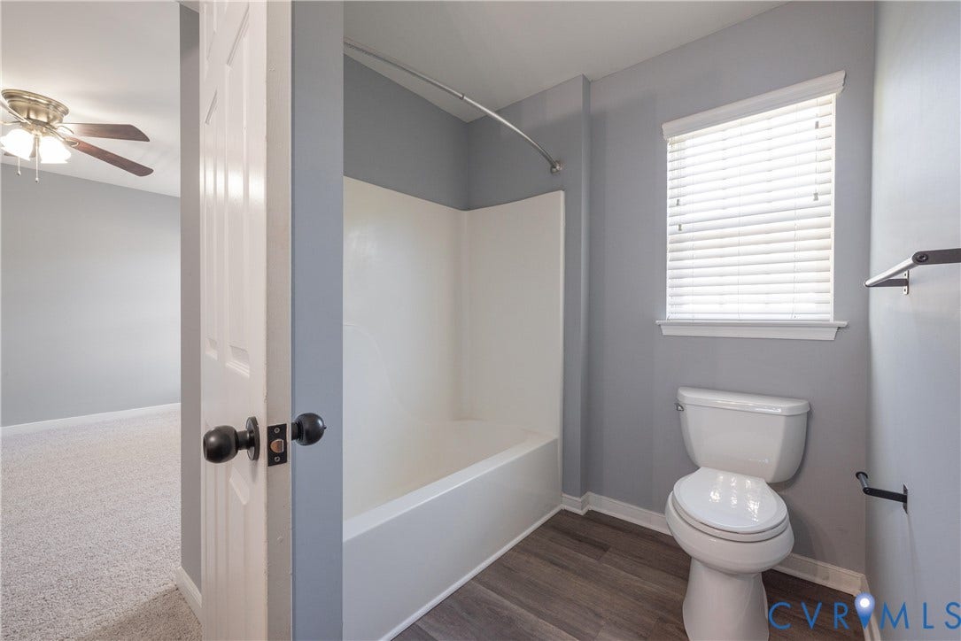 Bathroom featuring a full tub/shower combination, window with blinds, and wood-finish flooring