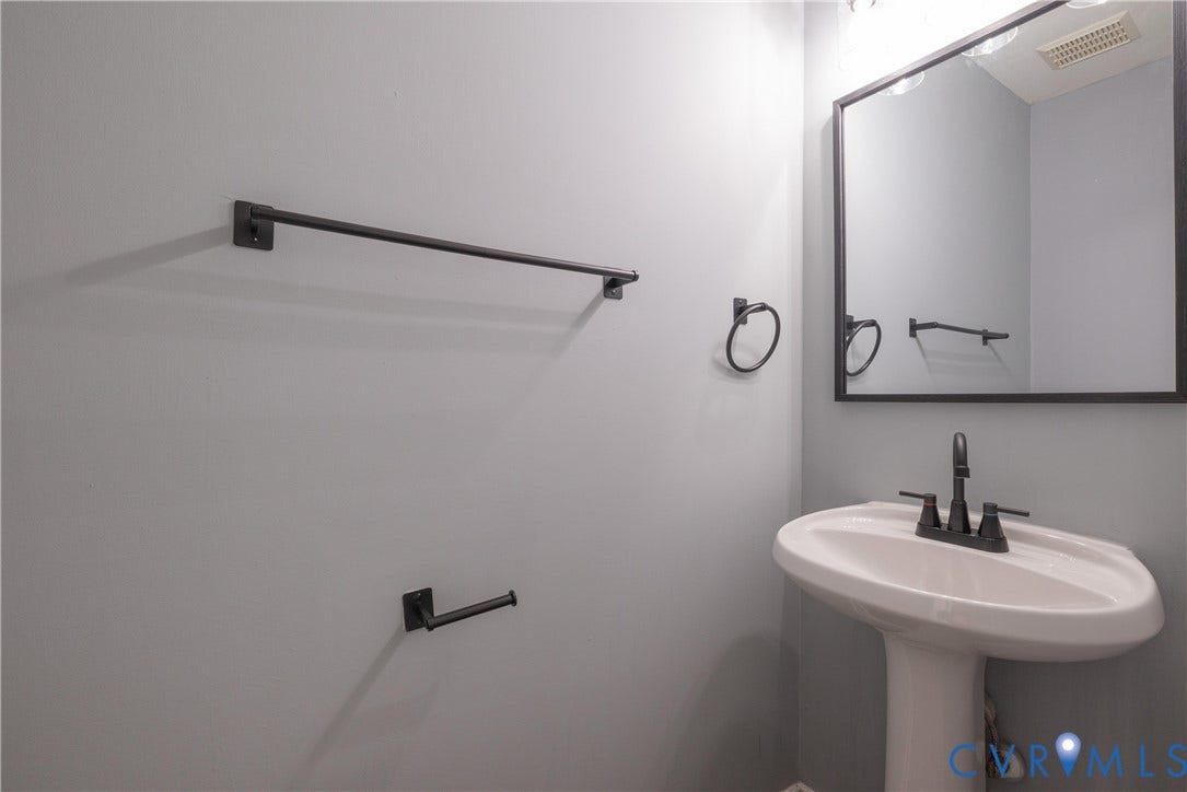 Powder Room with a pedestal sink with a matte black faucet, framed mirror, and coordinating matte black towel and toilet paper holders