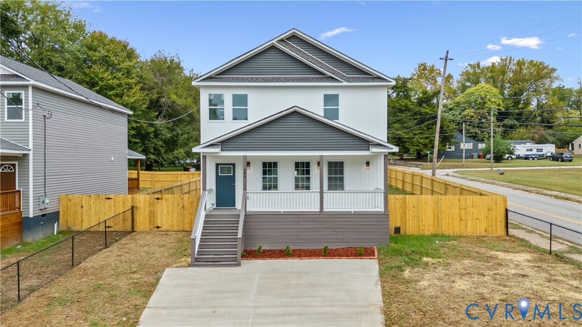 Two-story exterior with white and gray siding, front porch, concrete driveway, and wood privacy fencing
