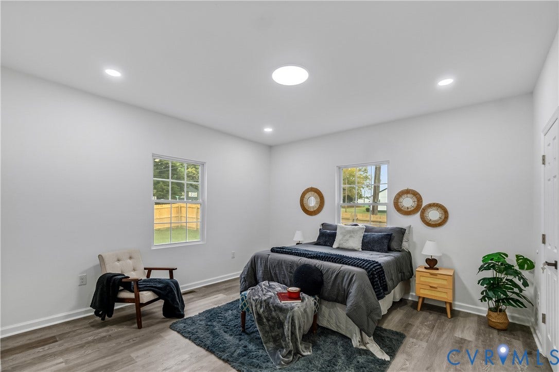 Recessed lighting, wood-finish flooring, two windows with white trim, and a white interior door