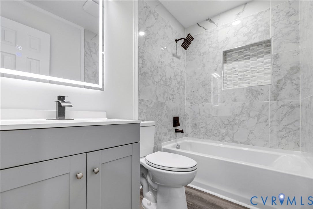 Modern bathroom featuring a lighted mirror, gray vanity with silver hardware, white countertop, and wood-finish flooring