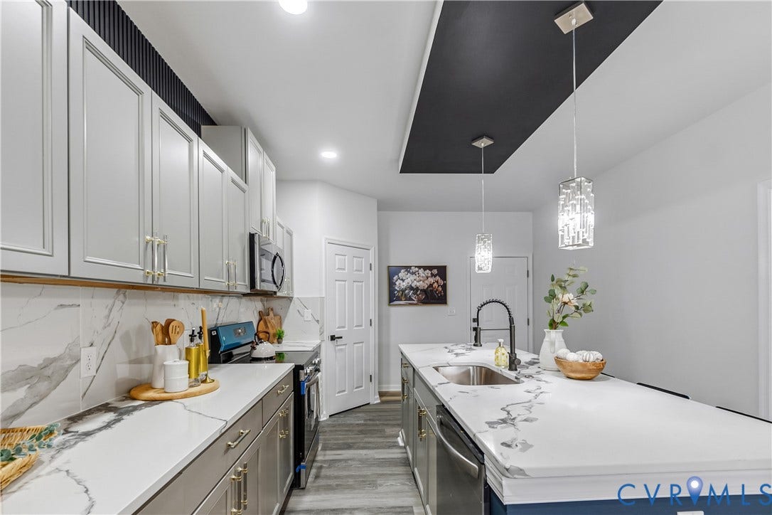 Kitchen featuring an extended island with a stainless steel sink, dual decorative pendant lighting, stainless steel appliances, white cabinetry with gold-tone hardware, and wood-finish flooring