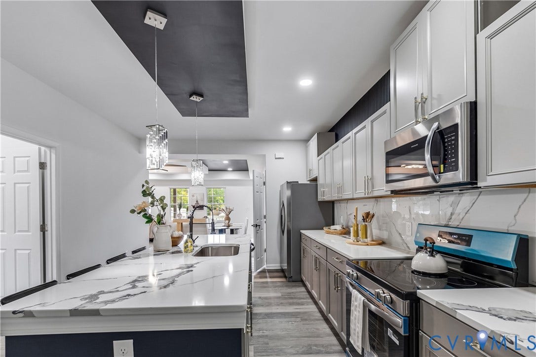 Kitchen featuring a large island with an undermount sink, quartz countertops, white upper cabinetry, gray lower cabinetry, and stainless steel appliances